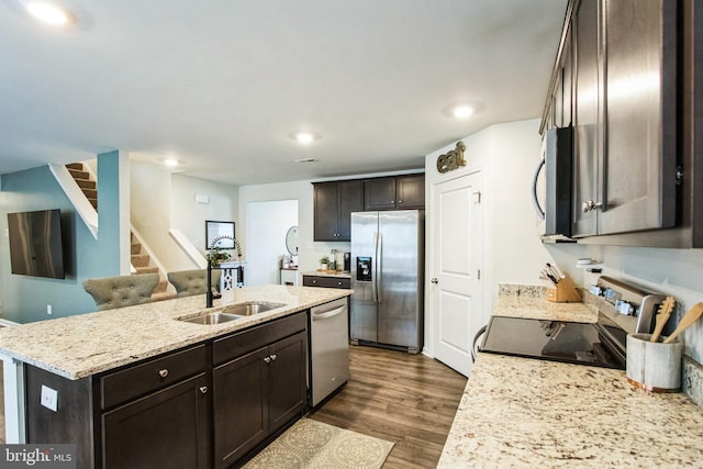 kitchen with a kitchen island with sink, stainless steel appliances, a sink, dark brown cabinets, and dark wood-style floors