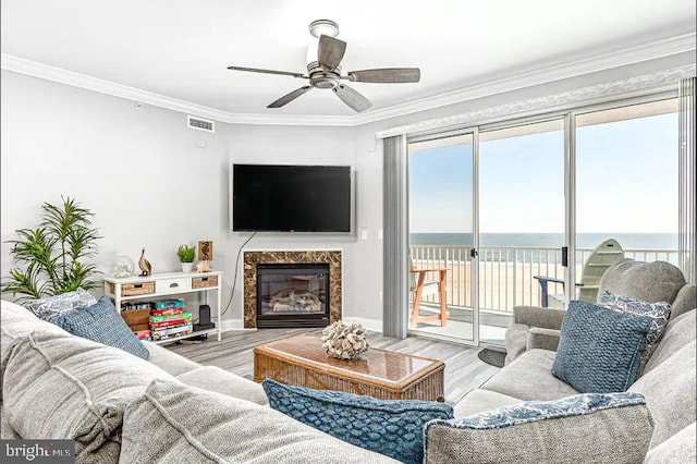 living room with ceiling fan, crown molding, a premium fireplace, and wood finished floors