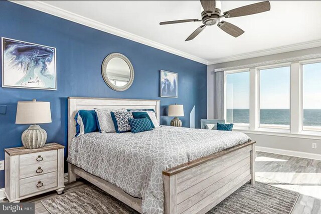 bedroom with a water view, crown molding, baseboards, and wood finished floors