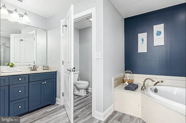 bathroom featuring a garden tub, toilet, vanity, wood finished floors, and baseboards