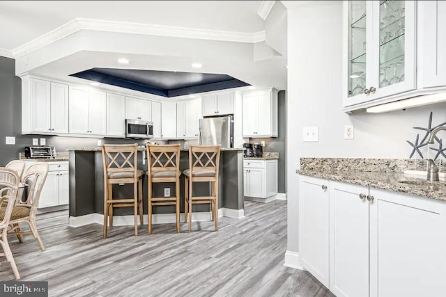 kitchen with appliances with stainless steel finishes, white cabinets, ornamental molding, and a kitchen breakfast bar