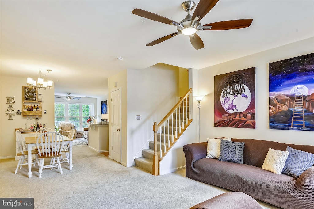 carpeted living room featuring ceiling fan with notable chandelier, baseboards, and stairs