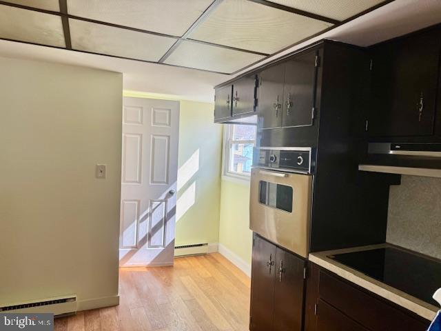 kitchen with black electric stovetop, light wood finished floors, a baseboard radiator, baseboard heating, and oven