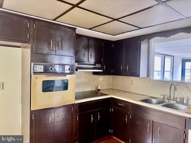 kitchen featuring light countertops, a sink, oven, under cabinet range hood, and black electric cooktop