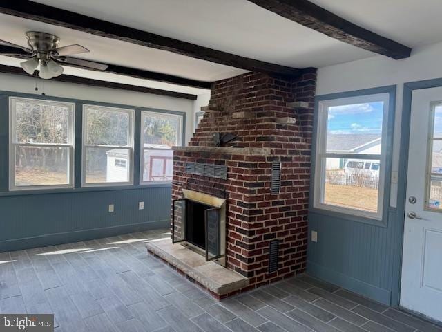 unfurnished living room with baseboards, ceiling fan, beamed ceiling, wood finish floors, and a fireplace