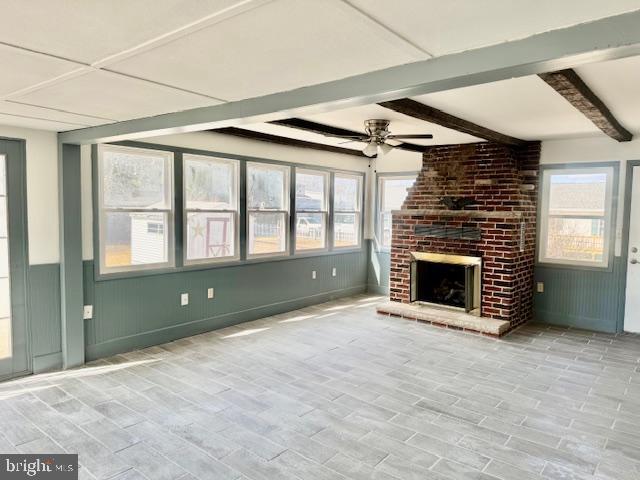 unfurnished living room featuring a wealth of natural light, beam ceiling, a fireplace, and ceiling fan