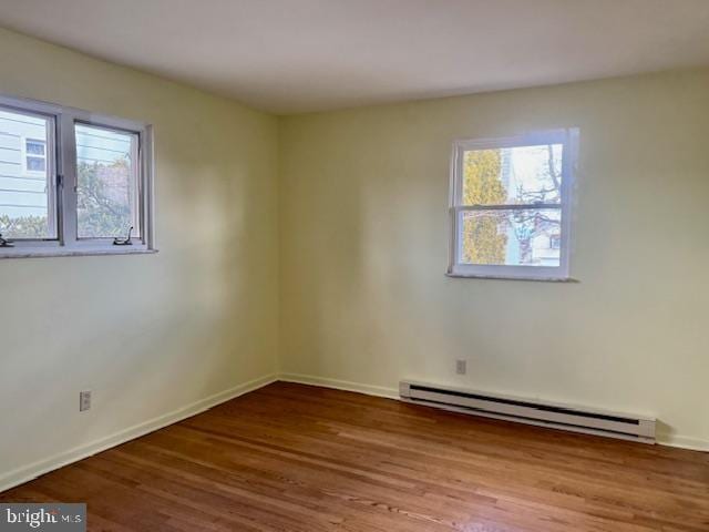 empty room with a baseboard radiator, wood finished floors, and baseboards