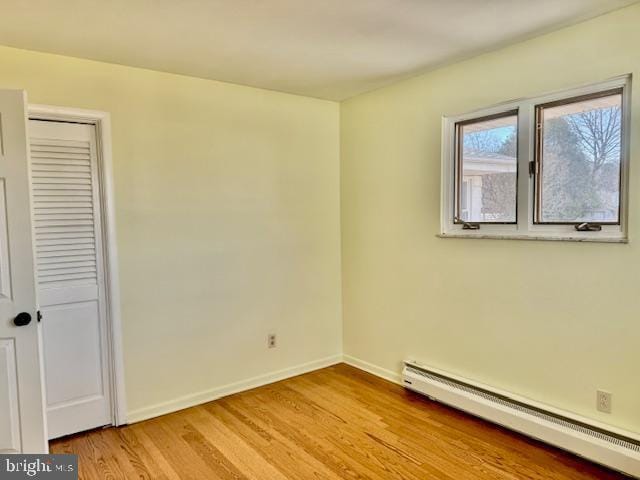 unfurnished room featuring a baseboard heating unit, baseboards, and light wood-style floors