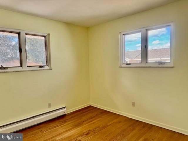 unfurnished room featuring baseboards, baseboard heating, and wood finished floors