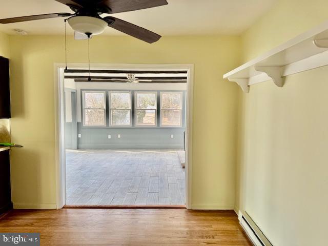 interior space with baseboards, ceiling fan, a baseboard heating unit, and wood finished floors