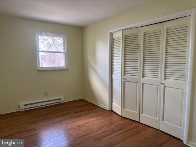 unfurnished bedroom featuring a closet, a baseboard heating unit, and wood finished floors