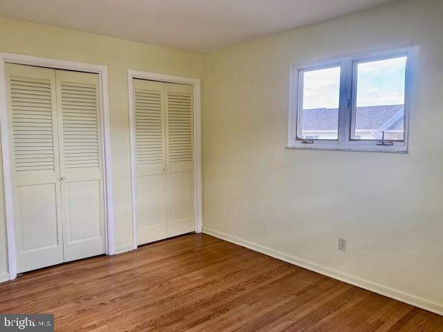 unfurnished bedroom with wood finished floors, two closets, and baseboards