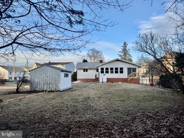 rear view of house featuring a lawn, a chimney, an outbuilding, fence, and a shed