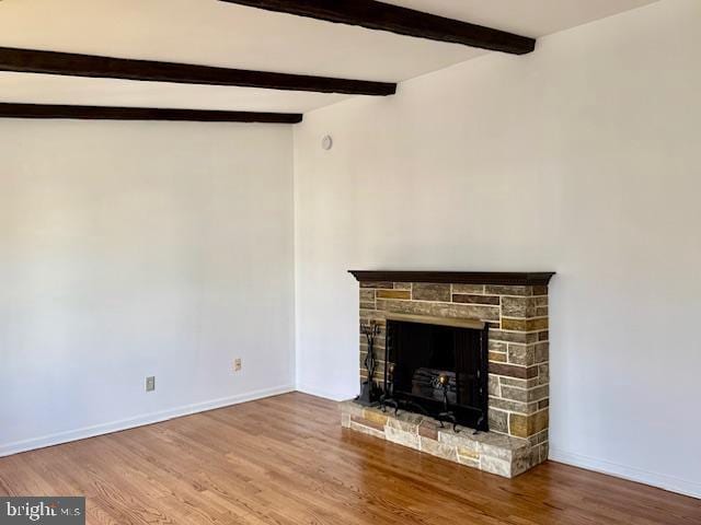 unfurnished living room with vaulted ceiling with beams, baseboards, wood finished floors, and a stone fireplace