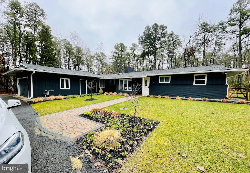 single story home featuring a front yard, an attached garage, a chimney, aphalt driveway, and board and batten siding