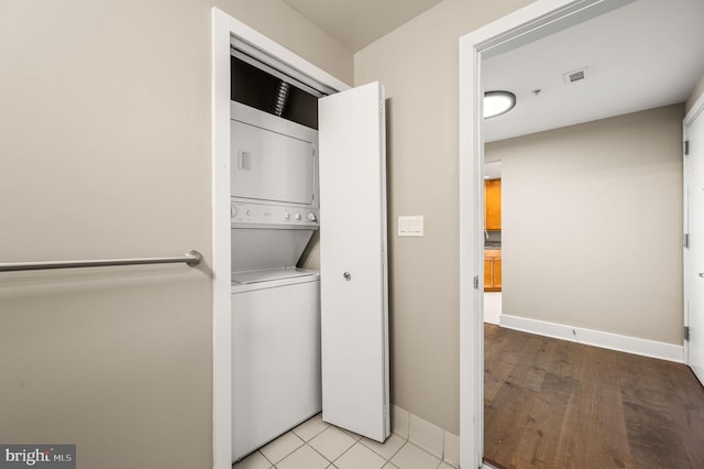 clothes washing area with visible vents, laundry area, stacked washer and clothes dryer, and baseboards