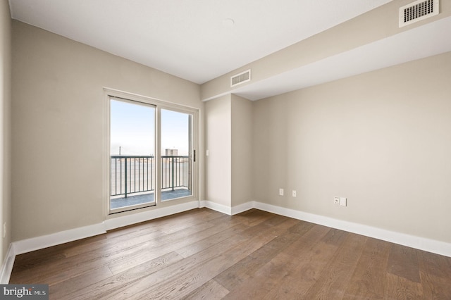 empty room featuring dark wood-type flooring, visible vents, and baseboards