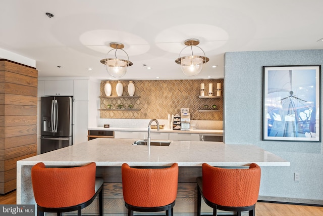 kitchen featuring light wood-style flooring, a kitchen island with sink, white cabinets, a sink, and stainless steel fridge