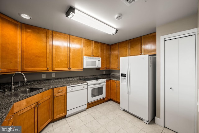 kitchen featuring white appliances, brown cabinetry, a sink, and light tile patterned flooring