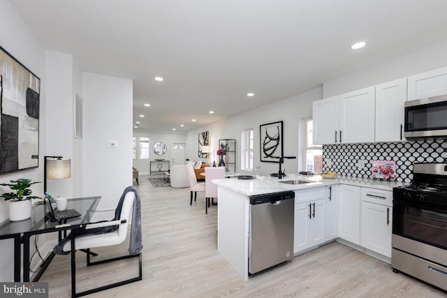 kitchen with appliances with stainless steel finishes, light wood-type flooring, white cabinets, and a sink