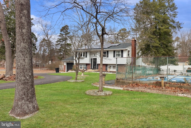 raised ranch with fence, driveway, solar panels, a chimney, and a front lawn