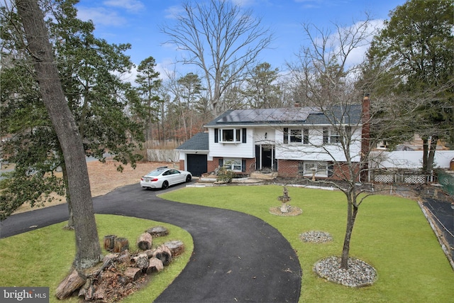 raised ranch with driveway, fence, a front yard, brick siding, and a chimney