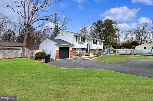 raised ranch featuring brick siding, fence, aphalt driveway, a front yard, and a chimney