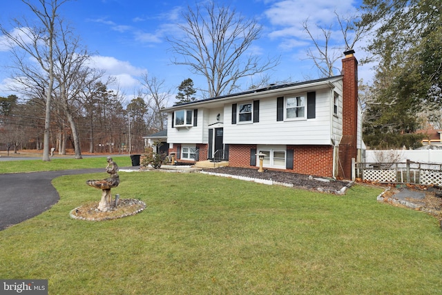 split foyer home with brick siding, a chimney, a front yard, and fence