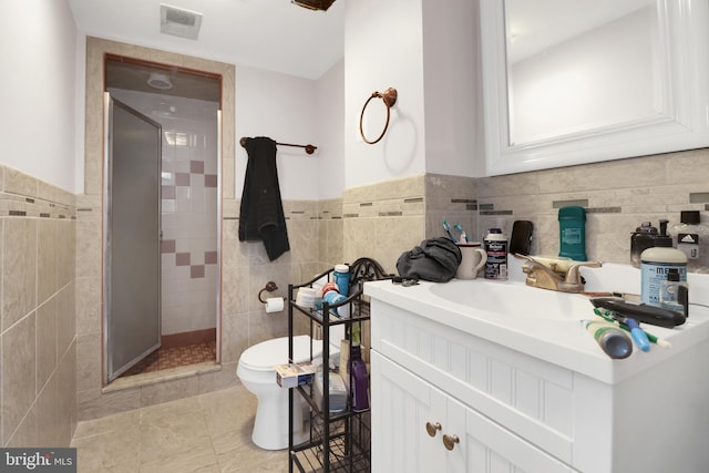 bathroom featuring visible vents, toilet, a stall shower, tile walls, and vanity