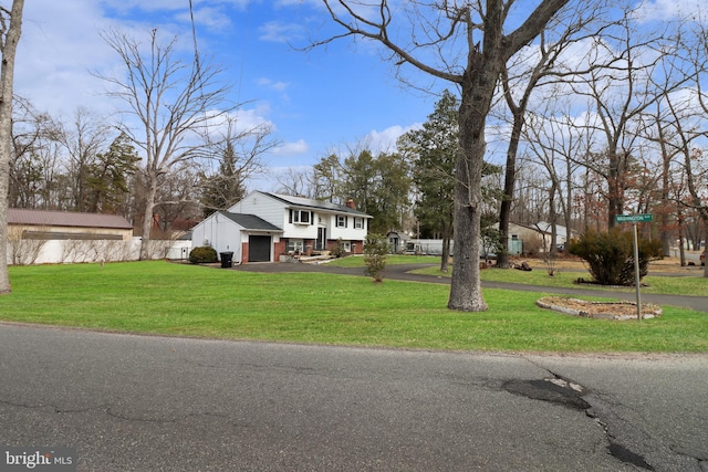 bi-level home featuring aphalt driveway, a chimney, a front yard, and brick siding