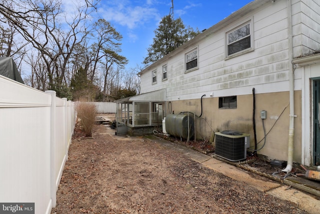 rear view of house with central AC unit, heating fuel, and fence