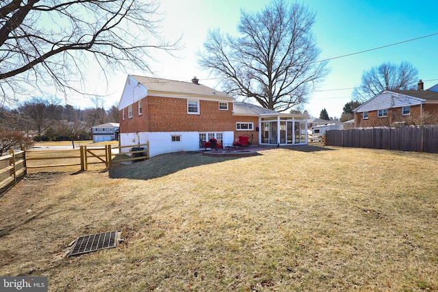 rear view of house with fence, a chimney, brick siding, and a sunroom