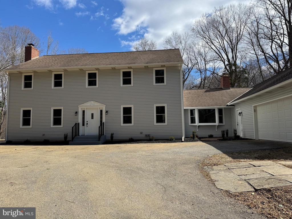 colonial inspired home with a garage, entry steps, driveway, and a chimney