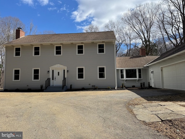 colonial inspired home with a garage, entry steps, driveway, and a chimney