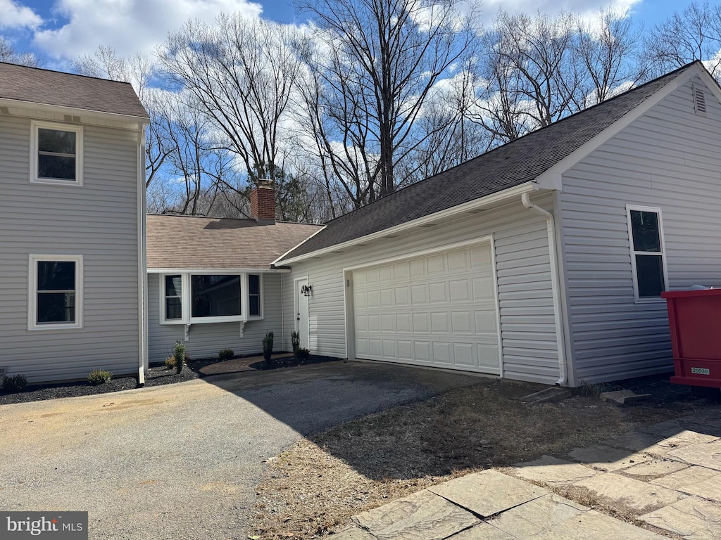 view of property exterior with an attached garage, a shingled roof, a chimney, and aphalt driveway