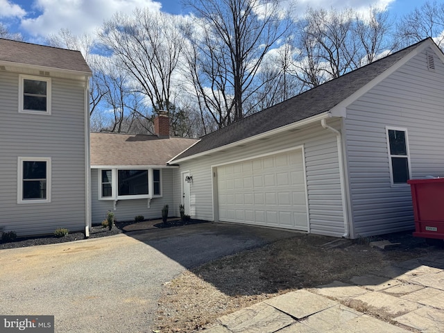 view of property exterior with an attached garage, a shingled roof, a chimney, and aphalt driveway