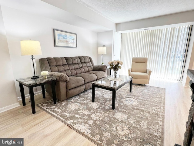 living area featuring light wood-type flooring, baseboards, and a textured ceiling