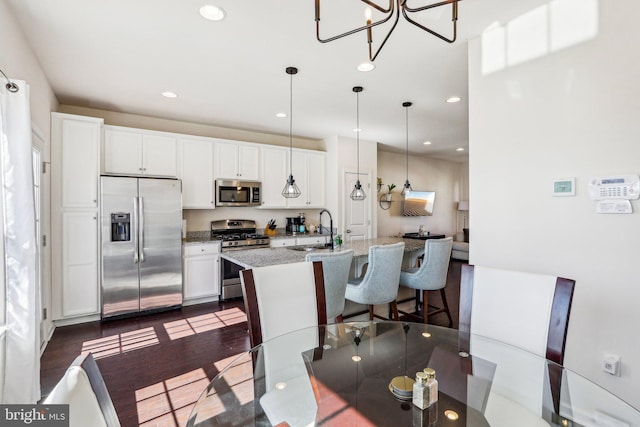 kitchen featuring a kitchen island with sink, stainless steel appliances, dark wood-type flooring, a sink, and white cabinets