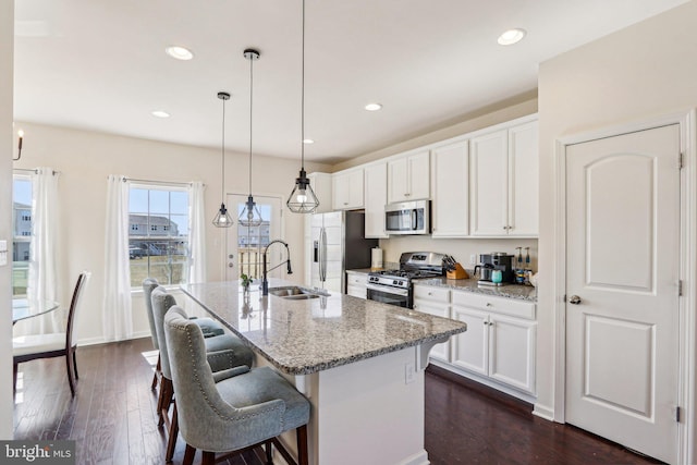 kitchen featuring a kitchen island with sink, stainless steel appliances, a sink, white cabinets, and dark wood-style floors