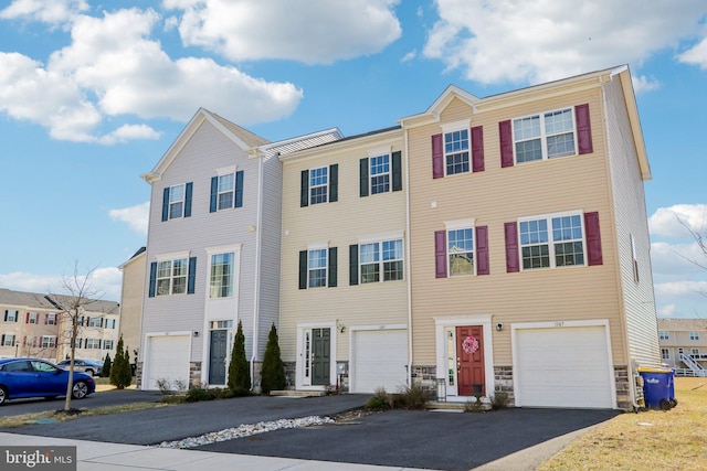 multi unit property with stone siding, driveway, and an attached garage