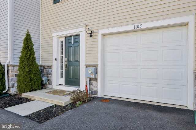 entrance to property with a garage, stone siding, and aphalt driveway