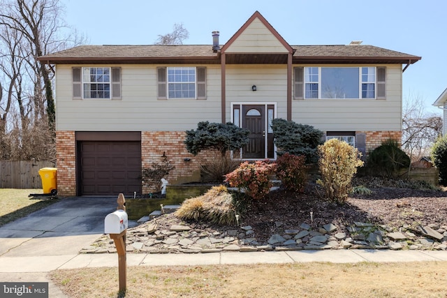 split foyer home with driveway, a garage, fence, and brick siding