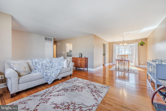 living room featuring light wood-type flooring, baseboards, visible vents, and a notable chandelier