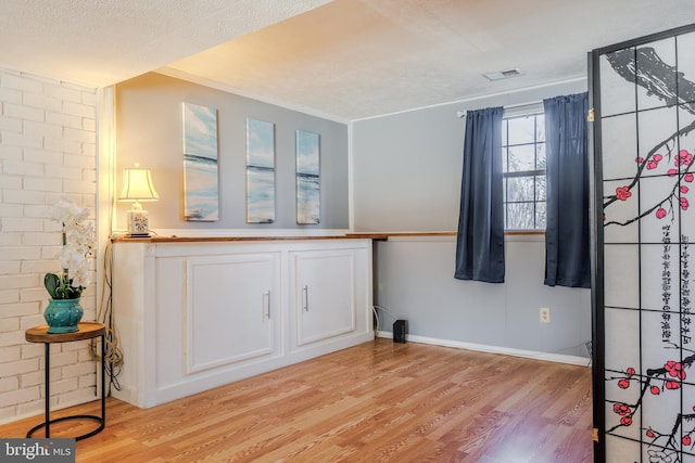 interior space featuring a textured ceiling, brick wall, visible vents, and light wood-style floors