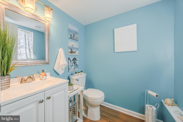 bathroom featuring visible vents, toilet, vanity, wood finished floors, and baseboards