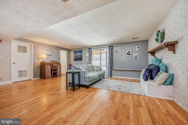 living area with a textured ceiling, wood finished floors, visible vents, and baseboards