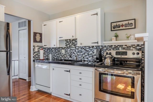 kitchen with decorative backsplash, dark countertops, stainless steel appliances, white cabinetry, and a sink