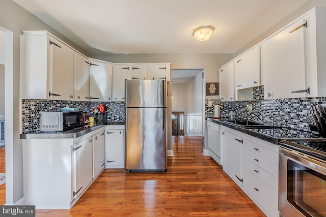 kitchen featuring dark countertops, appliances with stainless steel finishes, white cabinets, a sink, and wood finished floors