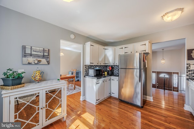 kitchen featuring black microwave, white cabinets, decorative backsplash, and freestanding refrigerator