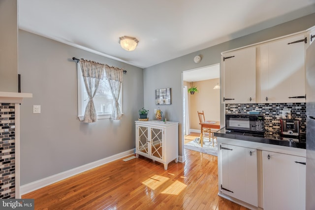 kitchen with light wood finished floors, tasteful backsplash, baseboards, and white cabinets